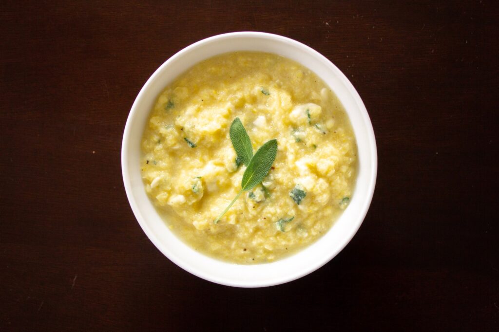 A bowl of yellow sweet corn polenta with fresh sage on top. 
